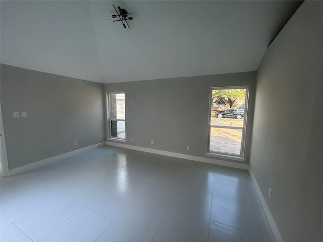 unfurnished room with vaulted ceiling, a wealth of natural light, and baseboards