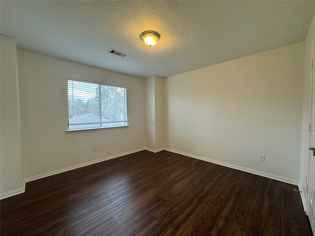 empty room featuring visible vents, dark wood finished floors, and baseboards