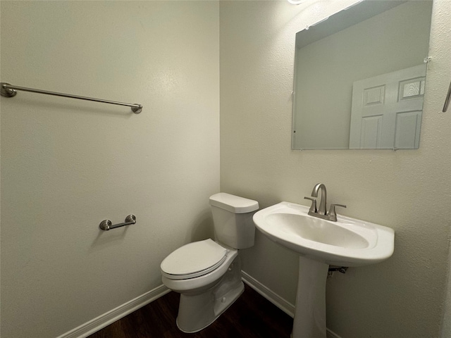 half bathroom featuring baseboards, a sink, toilet, and wood finished floors