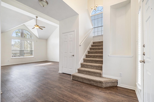 entryway with ceiling fan with notable chandelier, stairway, baseboards, dark wood-style flooring, and vaulted ceiling