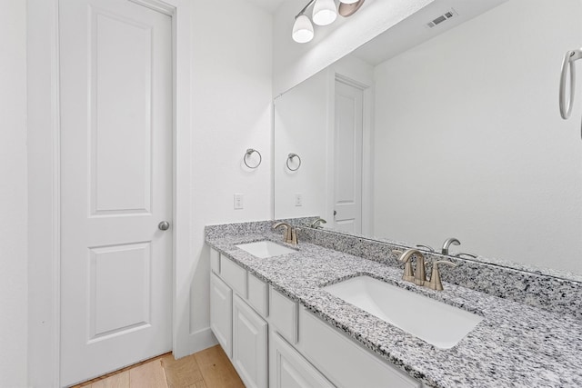 bathroom with double vanity, wood finished floors, a sink, and visible vents