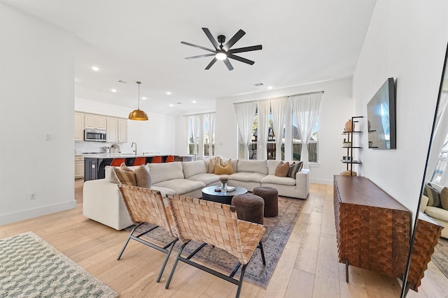 living room with light wood-style floors, baseboards, and a ceiling fan