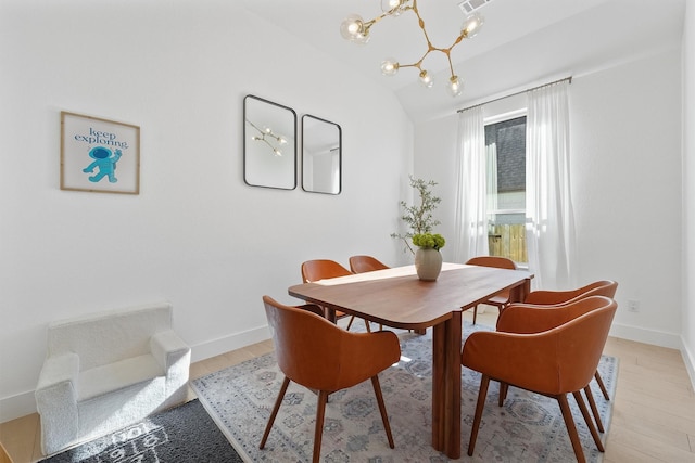 dining room featuring light wood finished floors, baseboards, vaulted ceiling, and an inviting chandelier