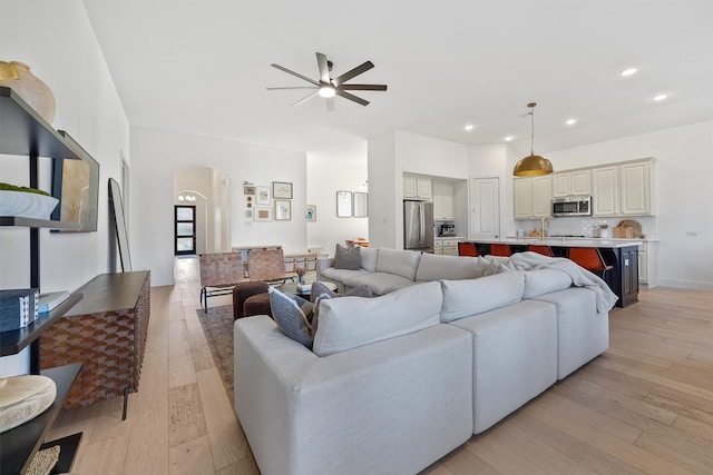 living room with a ceiling fan, arched walkways, light wood-style flooring, and recessed lighting