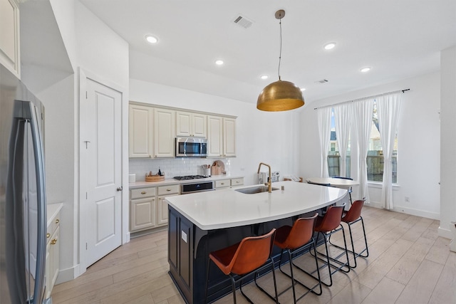 kitchen with stainless steel appliances, tasteful backsplash, visible vents, light wood-style floors, and a sink