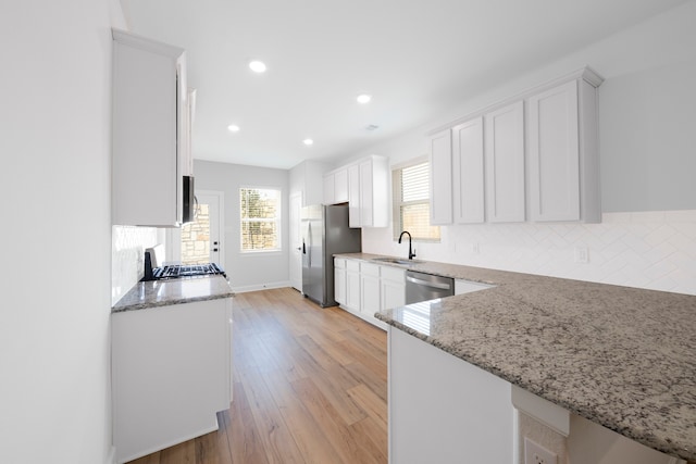 kitchen featuring stainless steel appliances, white cabinets, a sink, and light stone counters