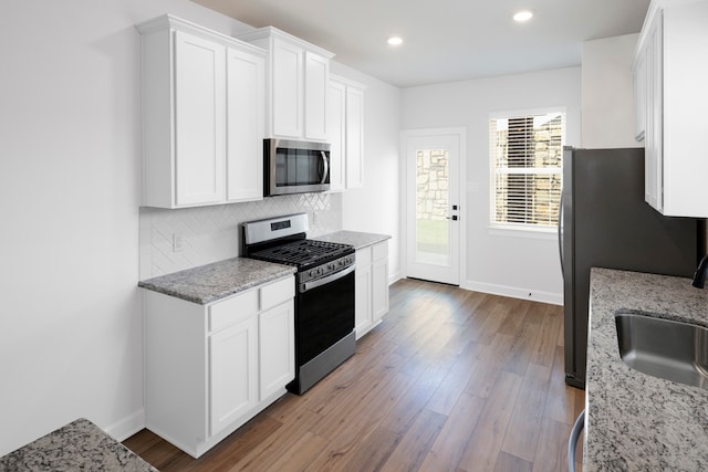 kitchen with light stone counters, stainless steel appliances, a sink, white cabinetry, and tasteful backsplash