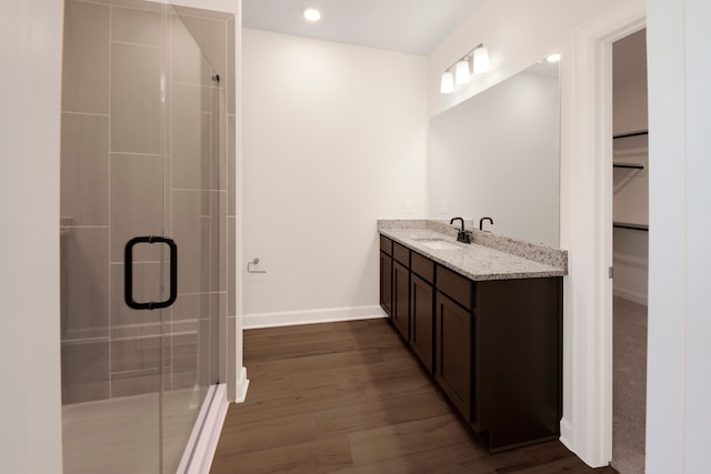 full bathroom with wood finished floors, a shower stall, vanity, and a walk in closet