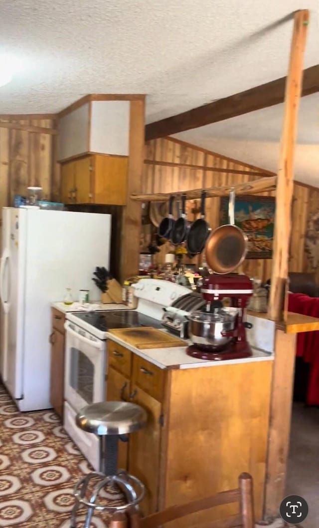 kitchen with white appliances, wooden walls, brown cabinets, vaulted ceiling with beams, and a textured ceiling