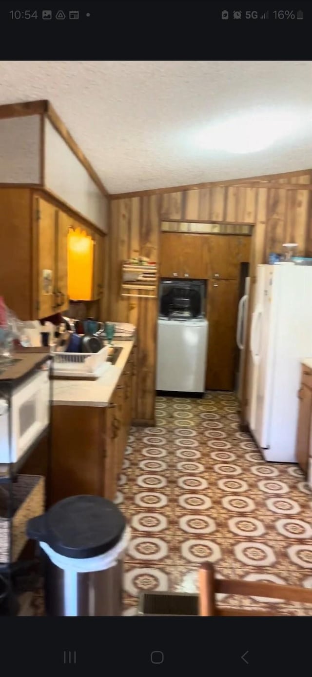 kitchen with brown cabinets, lofted ceiling, washer / clothes dryer, freestanding refrigerator, and wooden walls