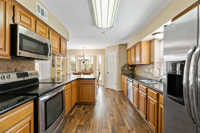 kitchen featuring dark wood finished floors, visible vents, appliances with stainless steel finishes, a sink, and a peninsula