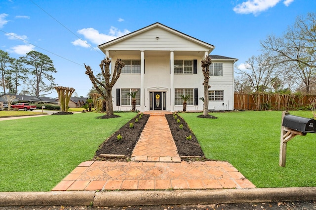 greek revival house with stucco siding, fence, and a front yard