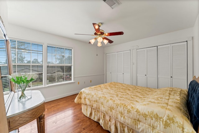 bedroom featuring ceiling fan, wood finished floors, visible vents, baseboards, and two closets