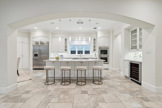 kitchen featuring wine cooler, stone tile floors, stainless steel appliances, a kitchen bar, and a center island with sink