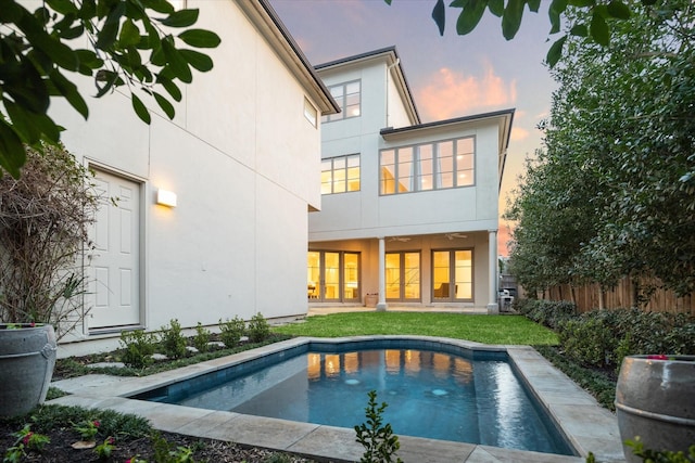 rear view of property with stucco siding, a lawn, and fence