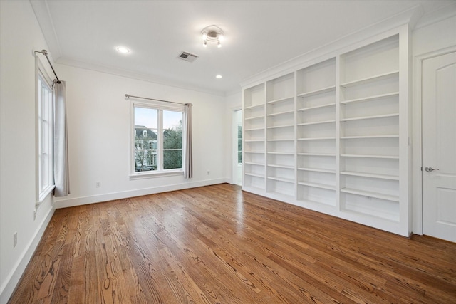 unfurnished room featuring built in features, baseboards, visible vents, wood finished floors, and crown molding