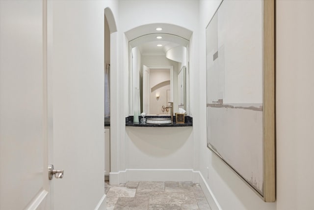 hall featuring baseboards, stone finish floor, arched walkways, and recessed lighting