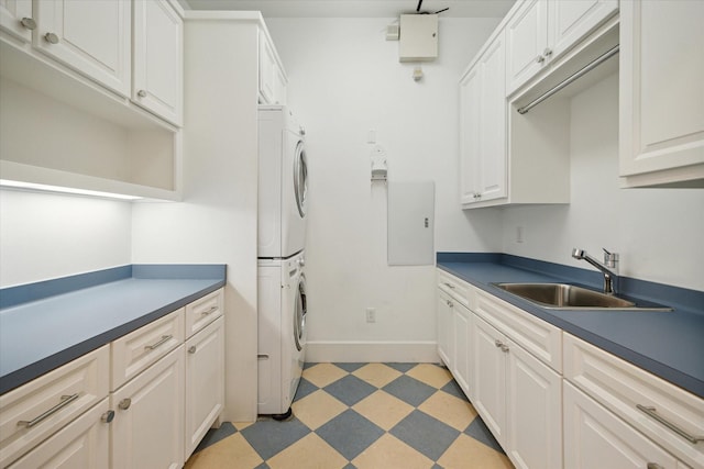 kitchen featuring stacked washer / dryer, dark countertops, light floors, white cabinetry, and a sink