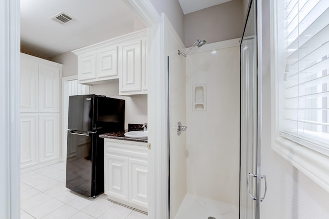 kitchen featuring visible vents, freestanding refrigerator, white cabinetry, a sink, and dark stone counters