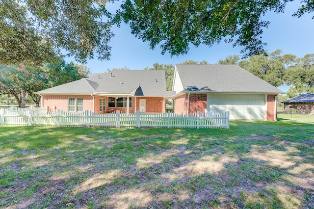 back of house with brick siding, a fenced front yard, an attached garage, and a lawn