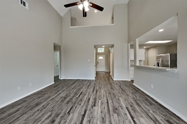 unfurnished living room featuring wood finished floors, a towering ceiling, a ceiling fan, visible vents, and baseboards