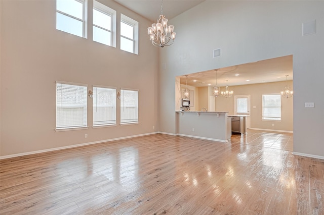 unfurnished living room with a notable chandelier, a high ceiling, visible vents, baseboards, and light wood finished floors