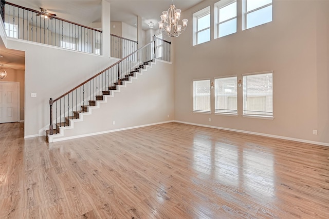 unfurnished living room with plenty of natural light, a notable chandelier, stairway, and light wood finished floors