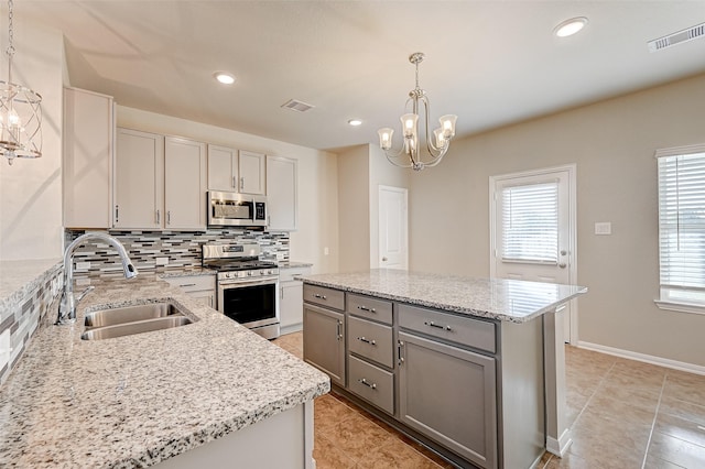 kitchen featuring a notable chandelier, gray cabinetry, stainless steel appliances, a sink, and tasteful backsplash