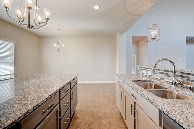 kitchen featuring light stone countertops, a notable chandelier, a sink, white cabinets, and decorative backsplash