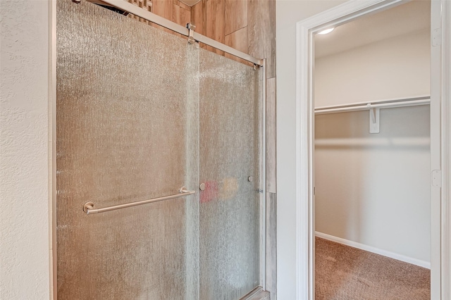 bathroom with a spacious closet, a shower stall, and baseboards