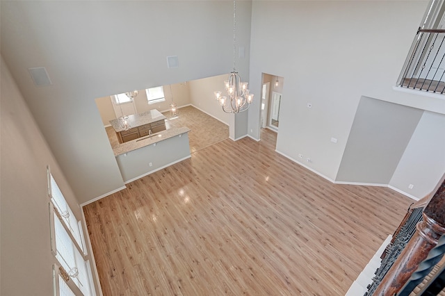 unfurnished living room featuring an inviting chandelier, a high ceiling, baseboards, and wood finished floors