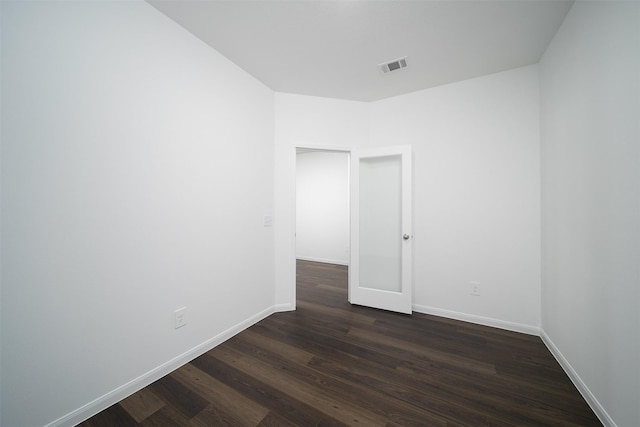 empty room with dark wood-style flooring, visible vents, and baseboards