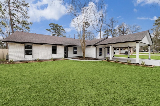 back of house with cooling unit, brick siding, a shingled roof, a lawn, and a carport