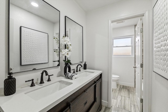 full bathroom featuring toilet, double vanity, baseboards, and a sink