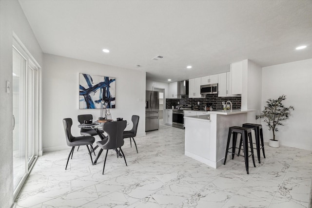 kitchen featuring a breakfast bar area, visible vents, backsplash, appliances with stainless steel finishes, and a peninsula