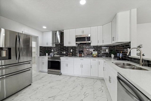 kitchen featuring stainless steel appliances, a sink, white cabinetry, marble finish floor, and wall chimney exhaust hood