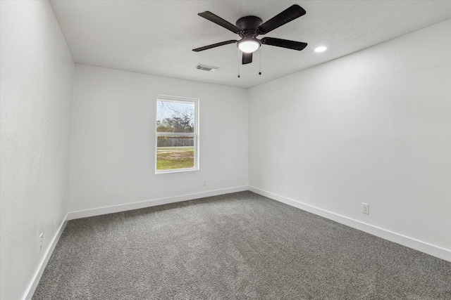 spare room with a ceiling fan, dark carpet, visible vents, and baseboards