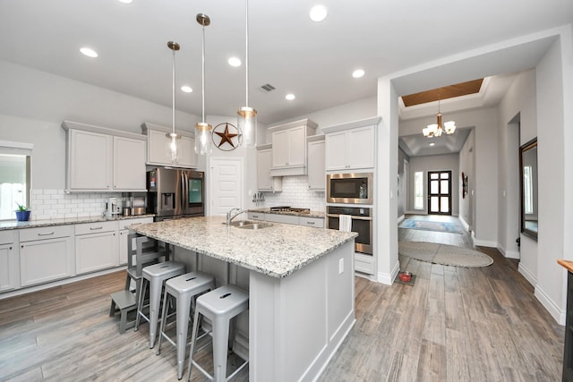 kitchen with visible vents, wood finished floors, a kitchen island with sink, stainless steel appliances, and a sink