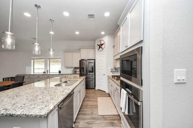 kitchen with stainless steel appliances, a spacious island, backsplash, a sink, and wood finished floors