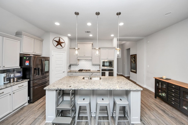 kitchen with decorative backsplash, appliances with stainless steel finishes, light wood-style floors, a kitchen island with sink, and a sink