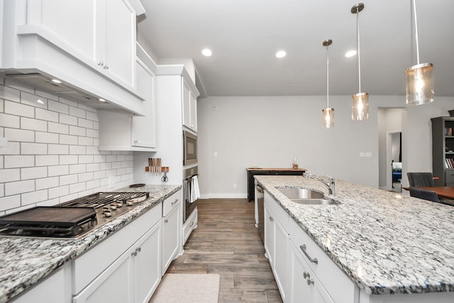 kitchen with decorative backsplash, appliances with stainless steel finishes, a kitchen island with sink, white cabinets, and a sink