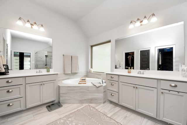 bathroom featuring a garden tub, a shower stall, vaulted ceiling, and two vanities