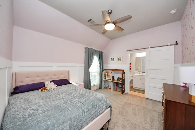 bedroom featuring a barn door, visible vents, light colored carpet, lofted ceiling, and a wainscoted wall