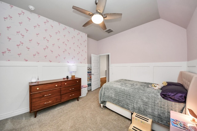 bedroom featuring lofted ceiling, ceiling fan, light carpet, wainscoting, and wallpapered walls