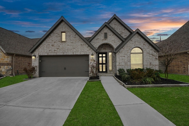 french country home featuring a garage, a front lawn, concrete driveway, and brick siding