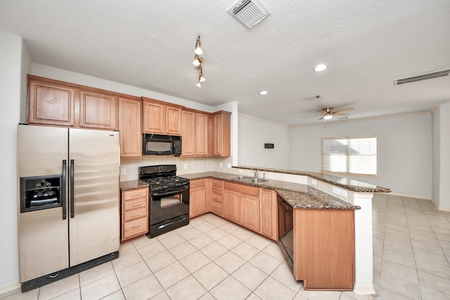 kitchen with visible vents, dark stone counters, a peninsula, black appliances, and a sink