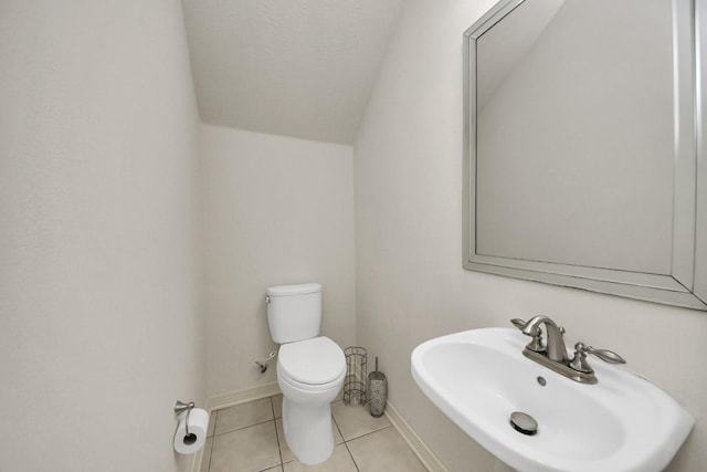 half bathroom featuring toilet, vaulted ceiling, a sink, baseboards, and tile patterned floors