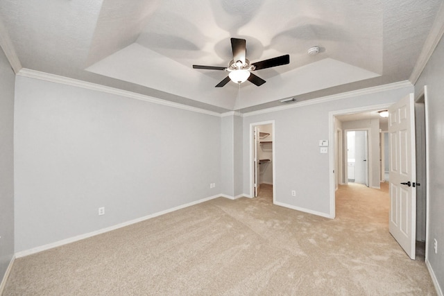 unfurnished bedroom featuring a walk in closet, baseboards, a raised ceiling, and crown molding