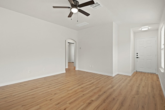 empty room with arched walkways, visible vents, ceiling fan, light wood-type flooring, and baseboards