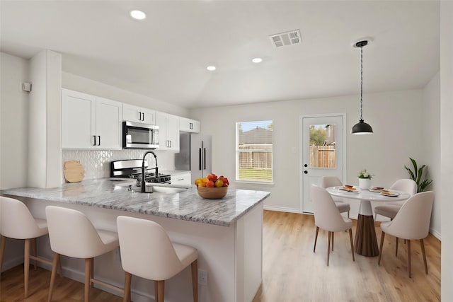 kitchen featuring appliances with stainless steel finishes, a kitchen breakfast bar, a peninsula, vaulted ceiling, and backsplash